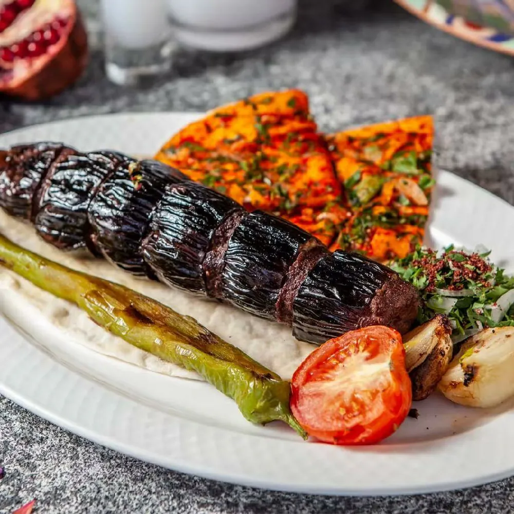 Urfa kebab with grilled pepper, tomato and onion on a white plate