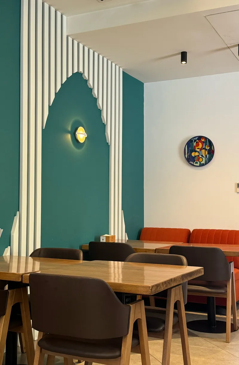 The indoor hall: a teal wall with a carved white arch and wooden tables