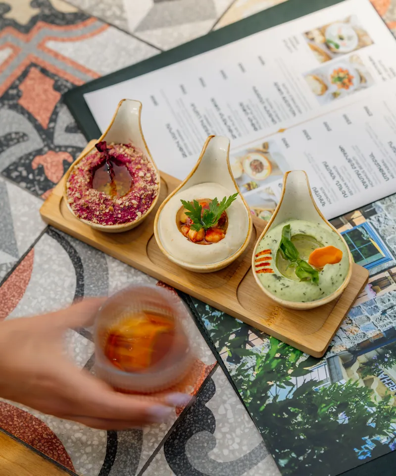 Mezze on a wooden board and a drink in hand over a painted tile table